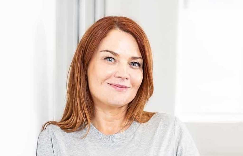 Sophie Jones, Chief Executive Officer at BWBF is smiling and leaning on a wall. She is wearing a pale grey top and her hair is dark red.