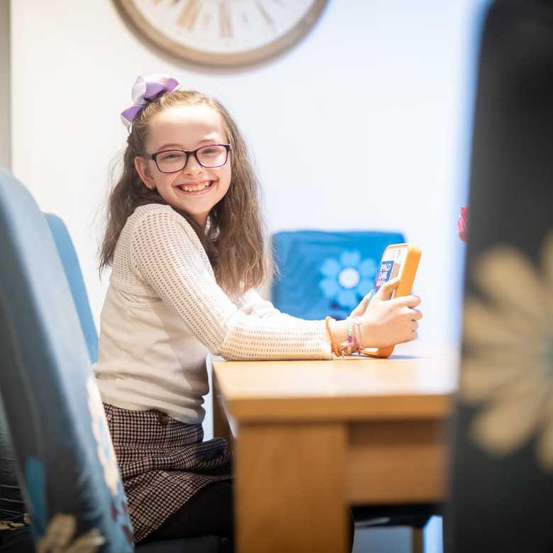BWBF service user Annabel sits at a table holding her Voxblock audio book reader. A copy of Roald Dahl's Matilda is inserted.