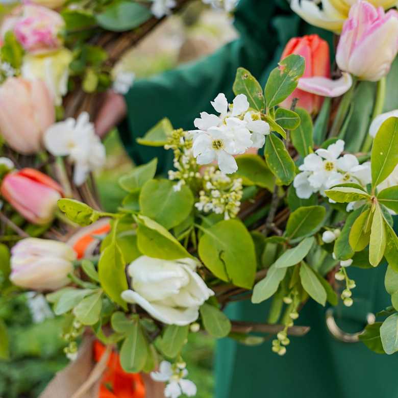 A person holds a funeral wreath with pink and white flowers.