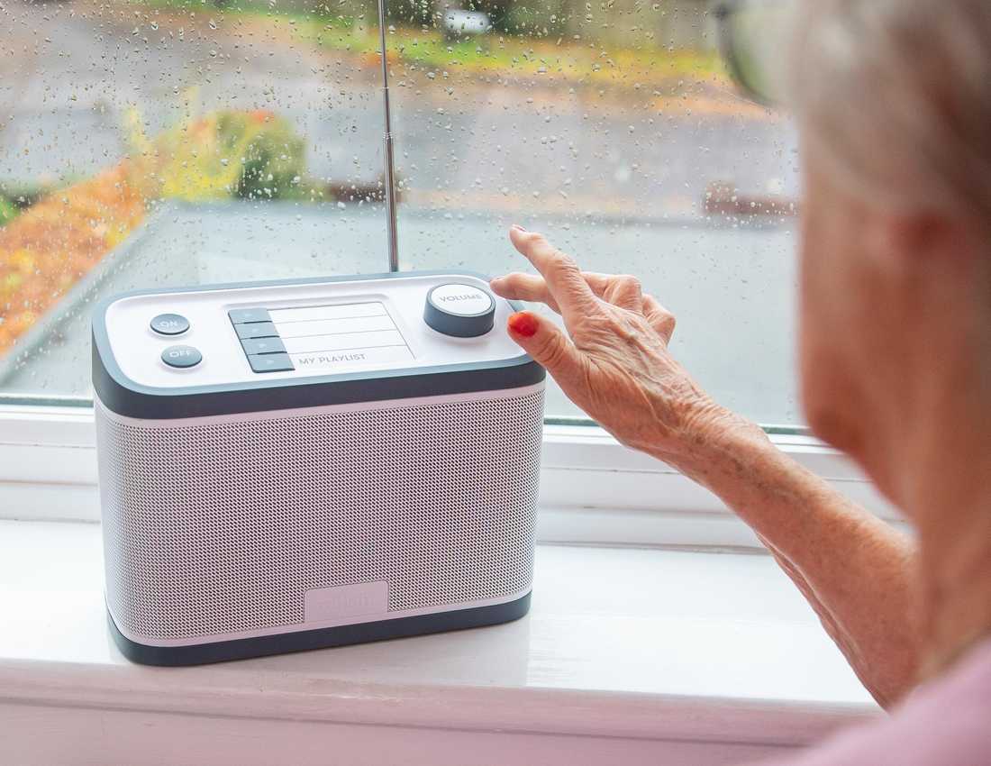 The Relish Radio sits on a windowsill as a user operates it. The radio is grey and white, with on/off button, four preset buttons and a volume control on top.