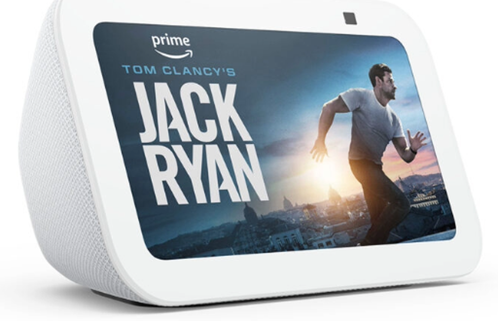 The Amazon Echo Show smart speaker. A white speaker with a rectangular screen at the front. The screen shows a promotional image for a Jack Ryan film.