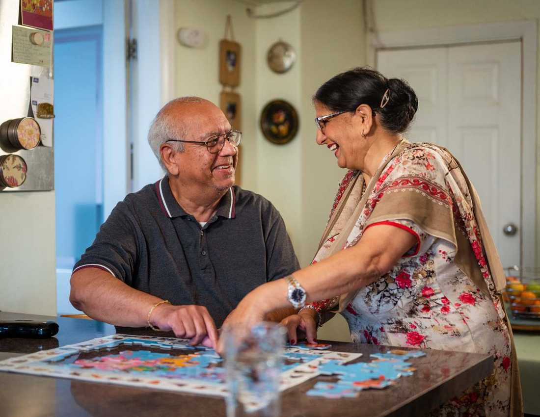 Older couple smiling at each other as they work on a jigsaw puzzle on their kitchen work top
