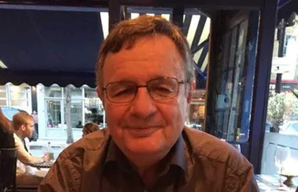 Paul Easton, who passed away in February 2023, is sitting smiling to camera. He wears glasses and has short dark hair.
