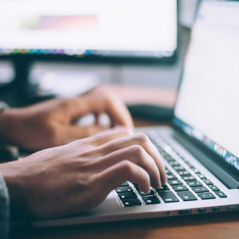 A close up of someone with a laptop computer, typing while the screen is lit up.