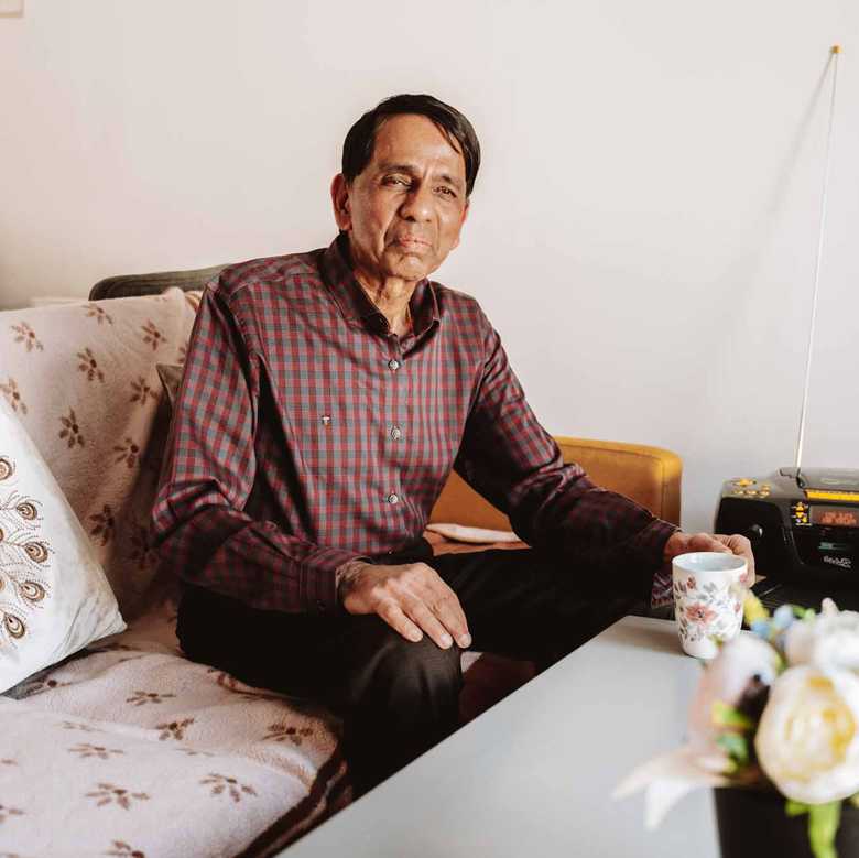 BWBF service user Krisha sits on a sofa. Next to him on a table is his Concerto 3 radio from BWBF.