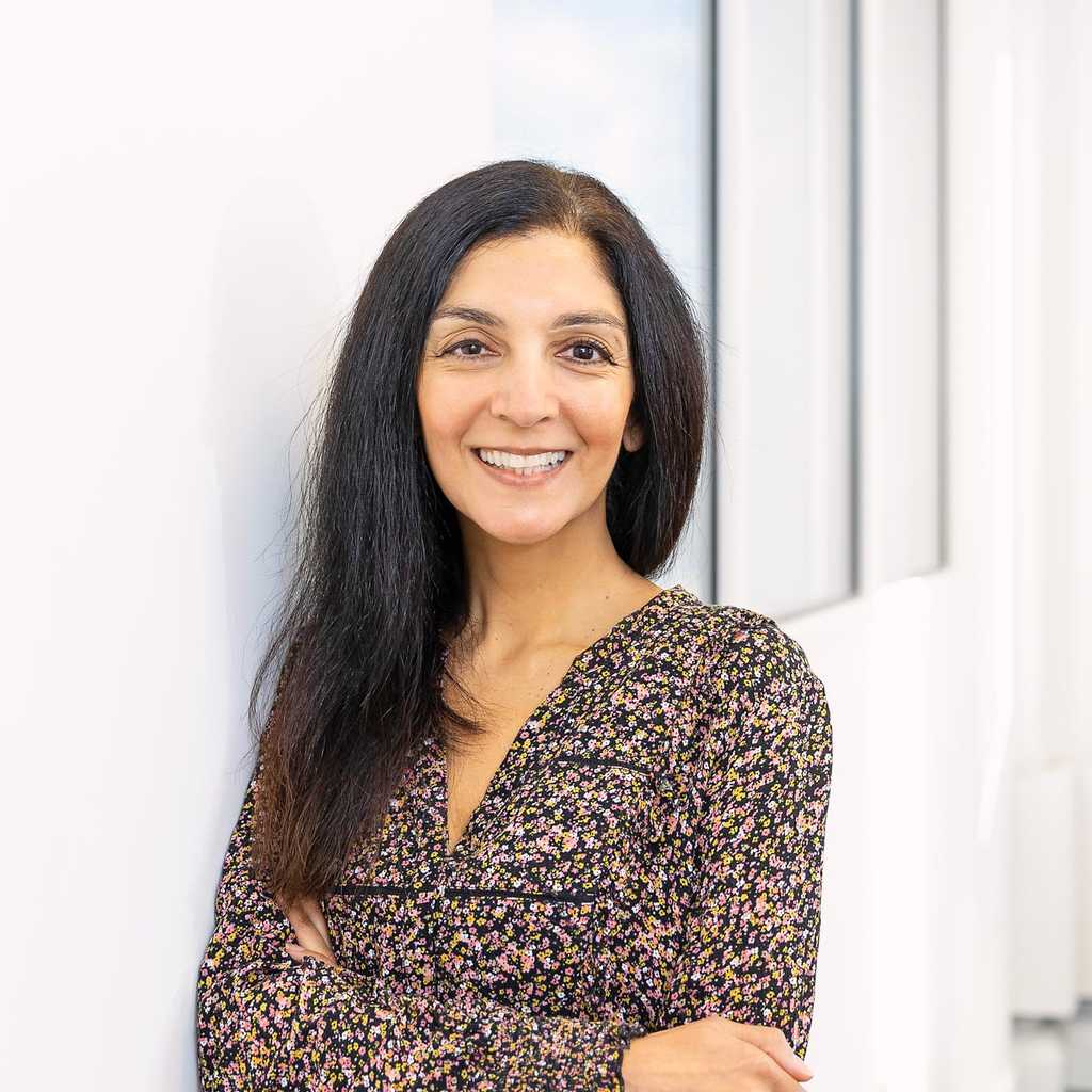 BWBF Communcations & Data Assistant Divya Kohli pictured in an office. She has her arms crossed and is smiling and wearing a brown floral dress.
