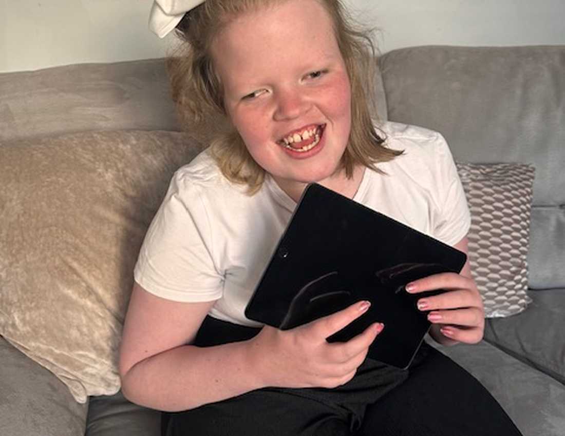 A photograph of Madison smiling broadly as she holds an iPad in her arms. She has a bow in her hair.