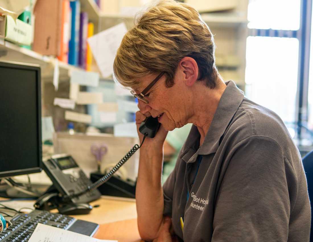 A volunteer with cropped hair and glasses sits at a desk with a phone in her hand.