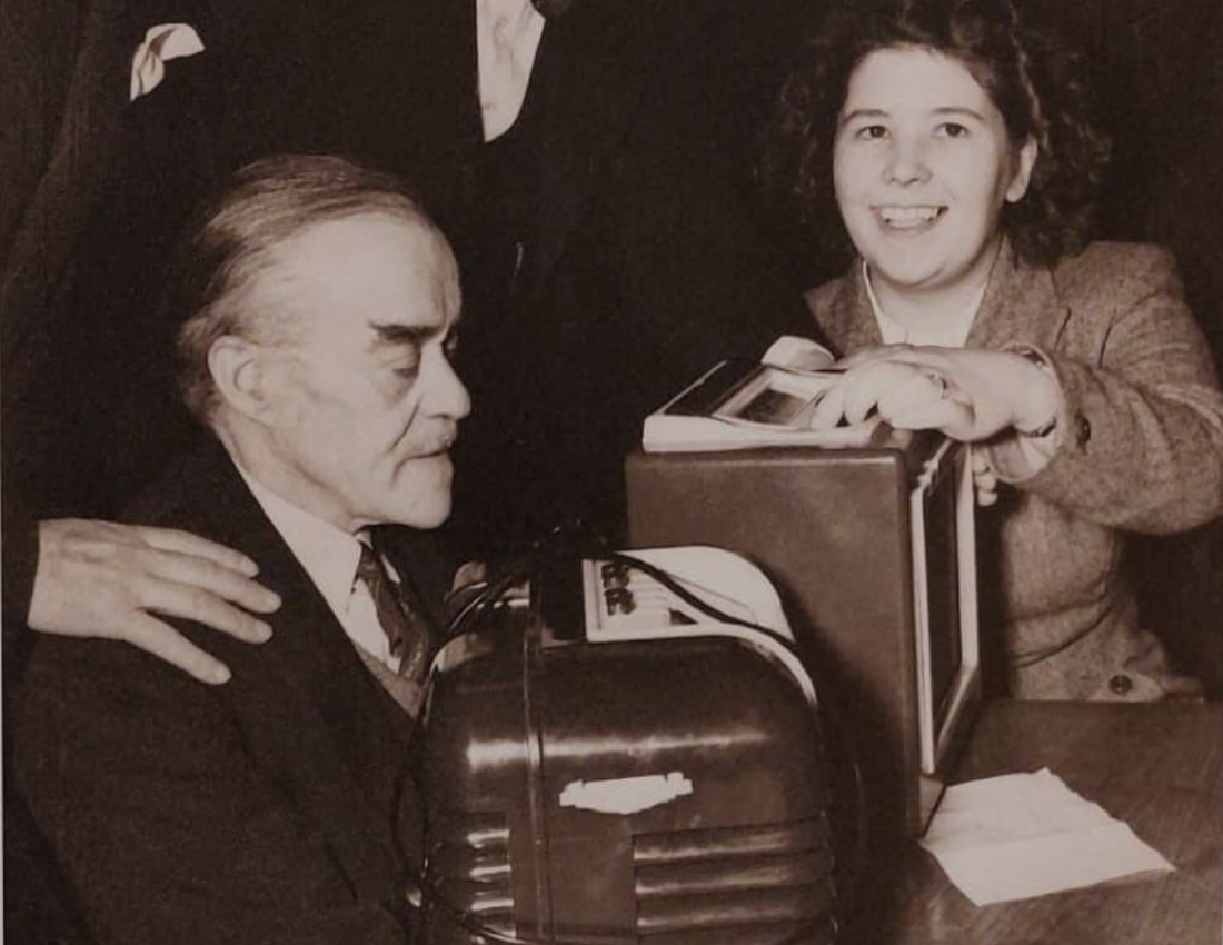 A black and white photo of people gathered around a Bush DAC10 radio, given to BWBF in the 1950s